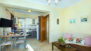 A compact living space with a dining area, kitchenette, and a sofa with decorative pillows. - Villa Jasmine Sostis by Villa Plus (Agios Sostis)