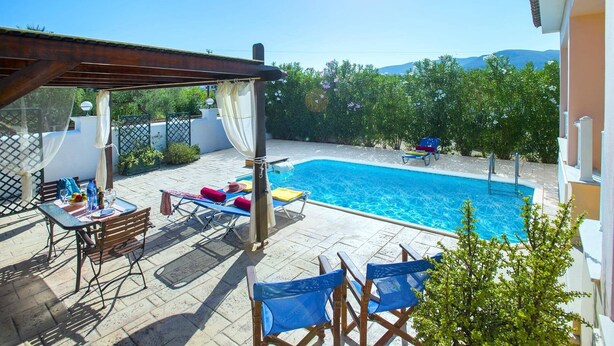 A pool area with a pergola, lounge chairs, and a table with drinks. - Villa Jasmine Sostis by Villa Plus (Agios Sostis)