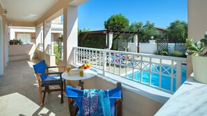 A balcony with a pool, two chairs, a table with drinks, and a view of the surrounding area. - Villa Jasmine Sostis by Villa Plus (Agios Sostis)