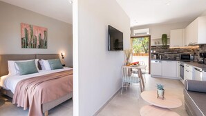 Una camera da letto moderna con un letto, un comodino e un quadro. La stanza si apre su una cucina con zona pranzo, TV e una finestra vista.