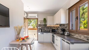 Cucina compatta con mobili bianchi, zoccolo in pietra e finestra vista verde.