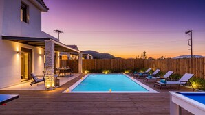 Una piscina con sillas de descanso y un área de comedor con mesa y sillas, rodeada por una terraza de madera y una valla de madera.