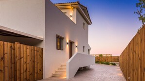 Una casa moderna con fachada blanca, cerca de madera y camino de hormigón que lleva a unas escaleras.