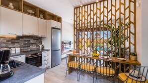 Una cocina moderna con armarios blancos, un refrigerador de acero inoxidable y un rebozado de ladrillo. Hay un comedor con sillas amarillas y una mesa de madera.