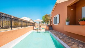 Une piscine dotée de chaises longues et d’un parasol, entourée d’une clôture et bordée d’un bâtiment avec une fenêtre.