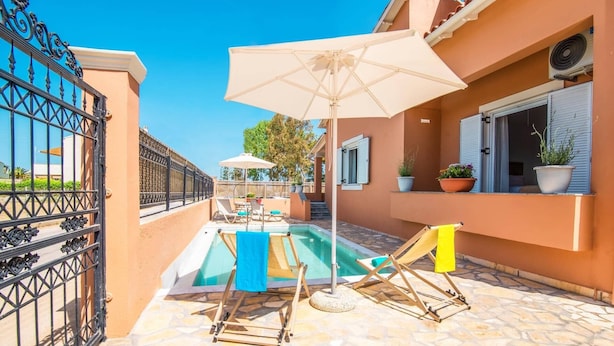 Un espace piscine aménagé avec des chaises longues et un parasol, entouré d’une terrasse en pierre et d’une clôture.