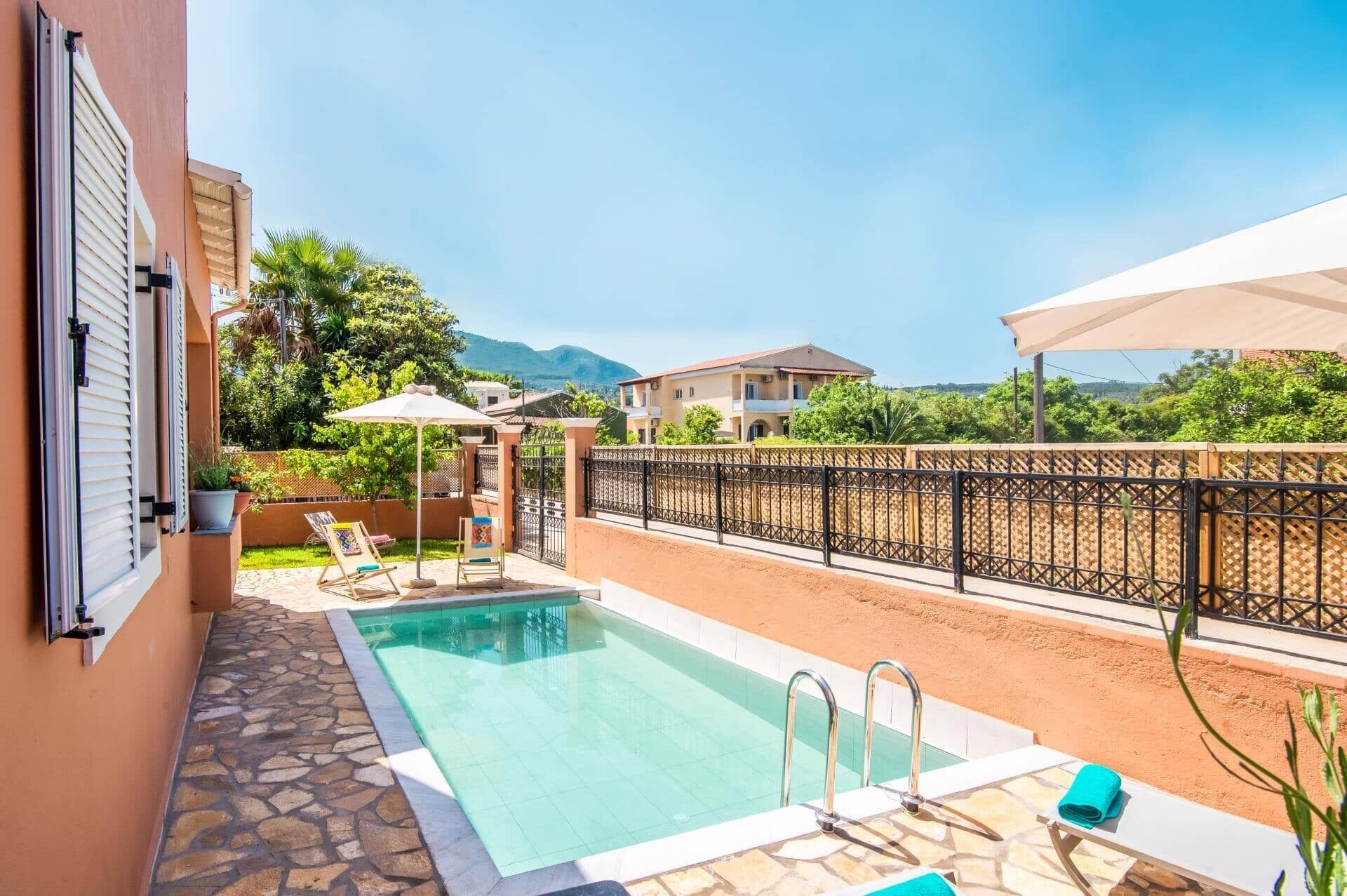 A swimming pool with a stone border, a covered seating area, and a view of a mountain in the background.