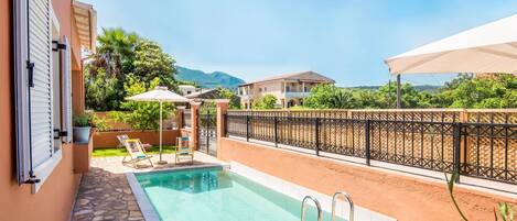 A swimming pool with a stone border, a covered seating area, and a view of a mountain in the background.