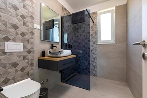 Un baño moderno con un salpicadero de azulejos geométricos, un espejo grande, un lavamanos con toalla y una zona de ducha.