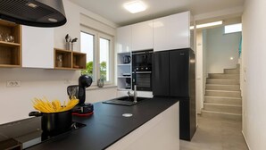 A modern kitchen with a black countertop, white cabinets, and a black refrigerator. There is a window providing natural light and a view of the outdoors. - Villa Lavandula by Villa Plus (Stokovci)