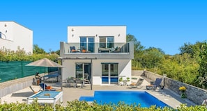 Una casa moderna de dos pisos con piscina, mobiliario exterior y un patio cubierto.