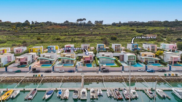 Een jachthaven met moderne, kleurrijke villa's en een steiger vol verschillende boten.