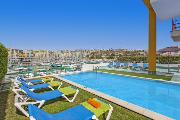 A swimming pool with lounge chairs and a view of a marina with boats.