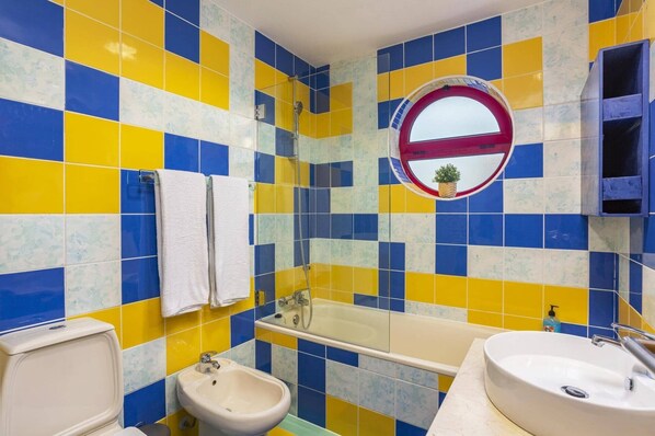 Un bagno con pavimento a scacchi blu e giallo, un bidet, una vasca da bagno e un lavandino.