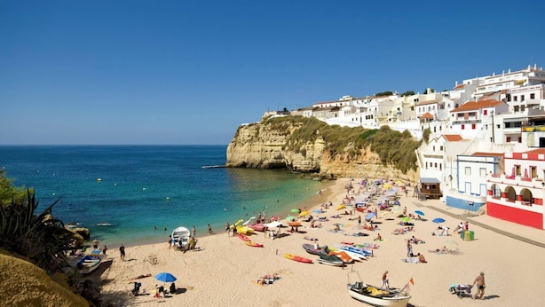 A beach with white buildings, clear blue sea, and people sunbathing. - Villa Maisie by Villa Plus (Praia do Carvoeiro)