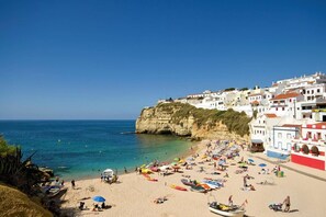 A beach with white buildings, clear blue sea, and people sunbathing. - Villa Maisie by Villa Plus (Praia do Carvoeiro)