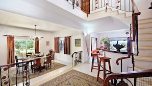 A spacious living area with a dining table, chairs, and a staircase with ornate railings. - Villa Maisie by Villa Plus (Praia do Carvoeiro)