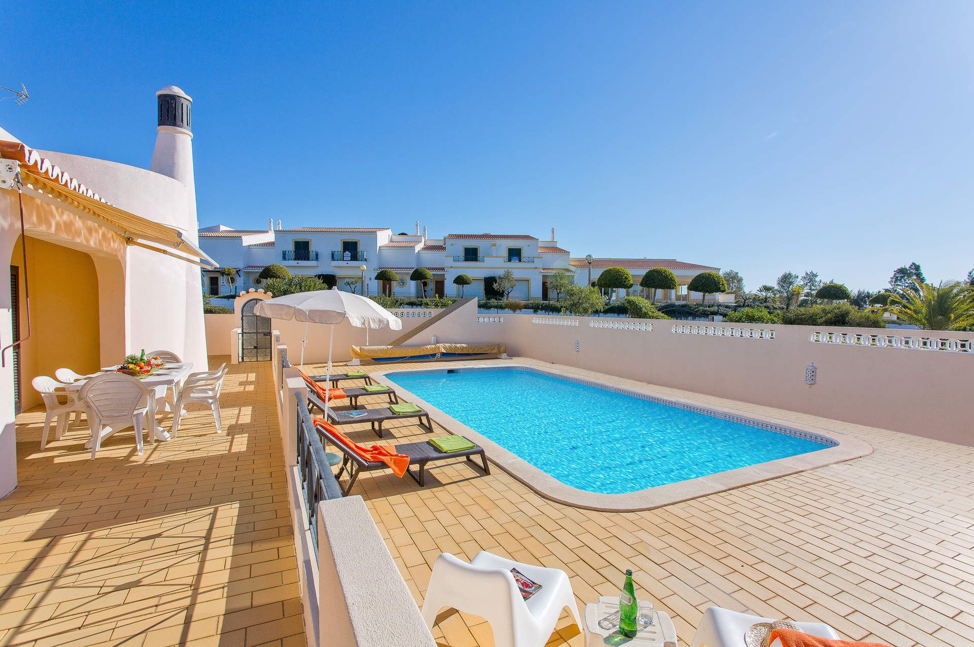 Uma área ao lado da piscina com piscina, espreguiçadeiras e uma mesa com uma garrafa.