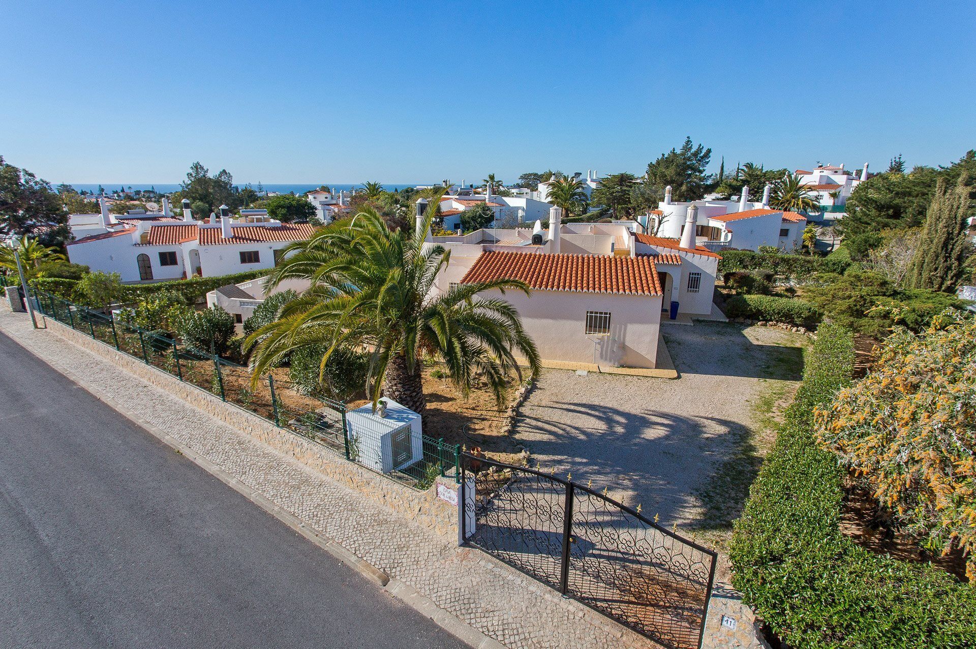 A coastal residential area with white buildings, red-tiled roofs, and a palm tree.