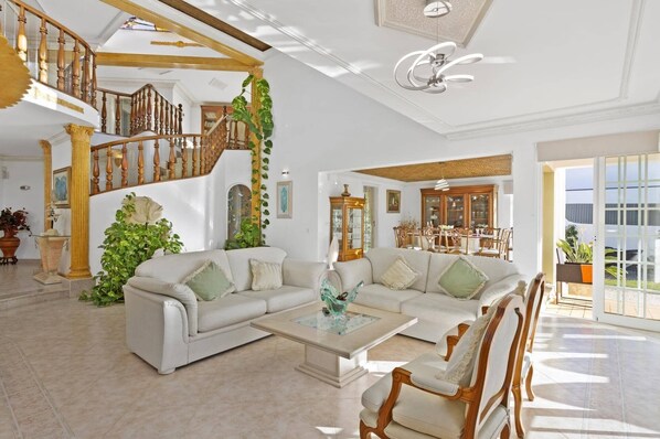 Uma sala de estar espaçosa com um sofá branco, uma mesa de centro e uma escada com corrimão de madeira.