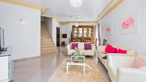 Un salón amplio con una escalera, una mesa de centro de vidrio y un sofá color beige con cojines rosa.