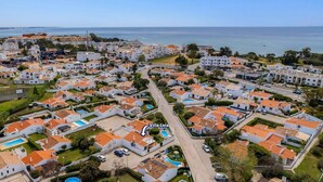 Vista aérea de una zona residencial costera con edificios blancos, techos anaranjados y una vista despejada del mar.