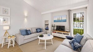 Una sala de estar moderna con un sofá, una mesa de centro y un mueble para televisión. Hay un balcón con vistas al mar.