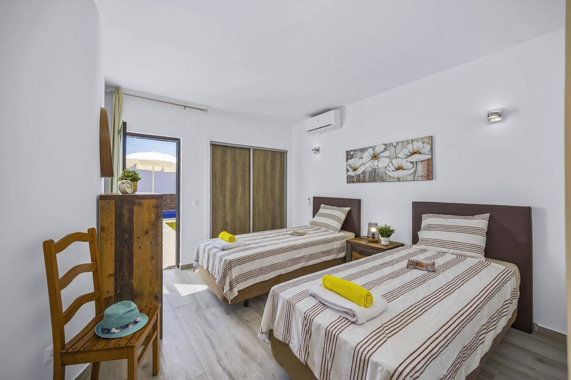 Ein Hotelzimmer mit zwei Betten, einem Holzstuhl, einem kleinen Tisch und einem Gemälde an der Wand.