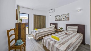 Habitación de hotel con dos camas, una silla de madera, una mesita y un cuadro en la pared.