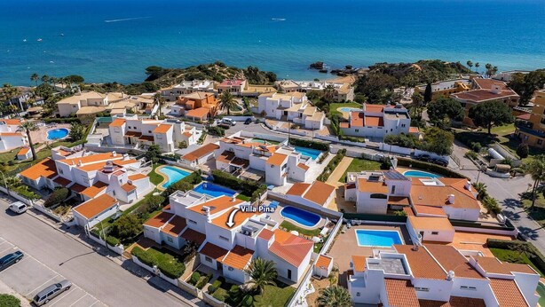 Vista aérea de una zona residencial costera con varias casas, cada una con piscina y vista al mar.
