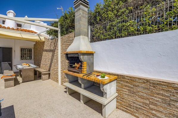 An outdoor kitchen with a chimney, stone walls, and a table set for dining.
