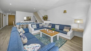 Una sala de estar moderna con un sofá azul, una mesa de centro de madera y una escalera que conduce a un nivel superior.