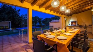 An outdoor dining area with a long table set for a meal, surrounded by wicker chairs, under a wooden ceiling with hanging lights. - Villa Miranda by Villa Plus (Albufeira)