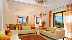 A spacious living room with a dining area, large windows, and a chandelier. - Villa Miranda by Villa Plus (Albufeira)