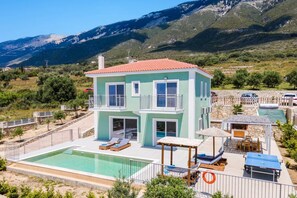 Un edificio di due piani con piscina, area salotto esterna e montagne sullo sfondo.