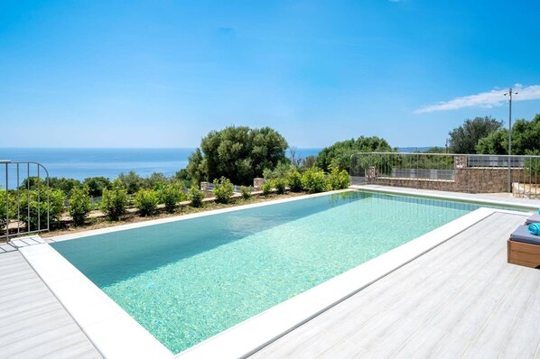 Una piscina rettangolare con acqua cristallina, circondata da un pontile in legno e una recinzione in metallo.