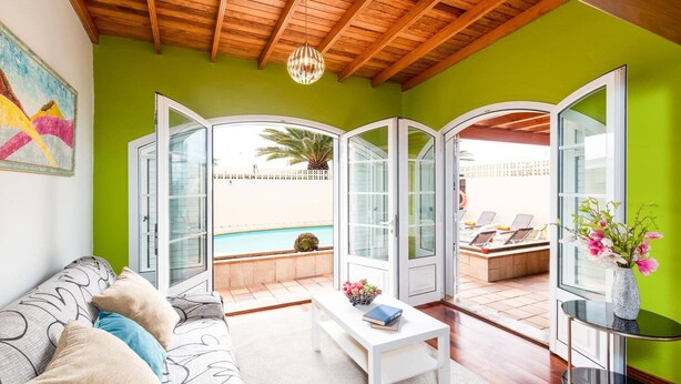 Une pièce lumineuse avec un mur vert, un plafond en bois et une grande fenêtre donnant sur une piscine.