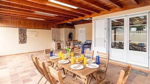 Un coin repas avec une table en bois dressée pour quatre personnes, entourée de chaises. On aperçoit un mur en pierre et une cheminée à l’arrière-plan.