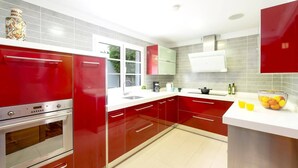 Une cuisine moderne avec des meubles de rangement rouges, un four en acier inoxydable et un plan de travail blanc.
