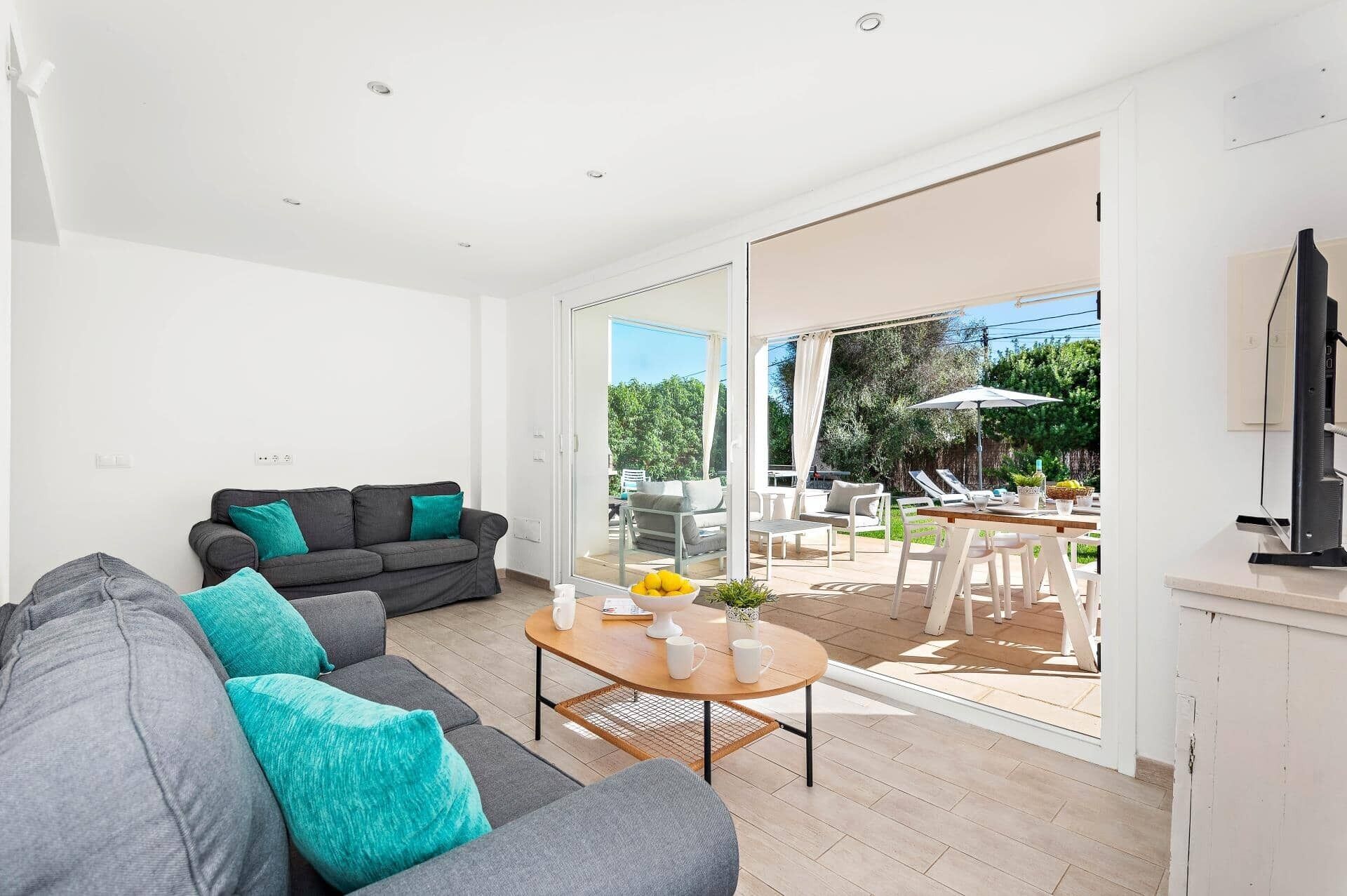 Uma sala de estar moderna com um sofá cinzento, uma mesa de centro e uma área de refeições com mobiliário para área externa.