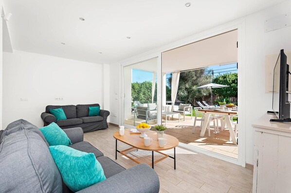 A modern living room with a grey sofa, a coffee table, and a dining area with outdoor seating.