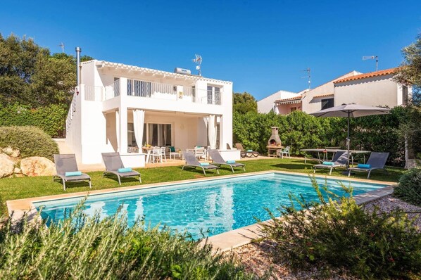 Eine zweistöckige Villa mit Swimmingpool, Sitzgelegenheiten im Freien und einer Grillgegend.