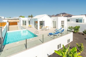Ein moderner Poolbereich auf dem Dach mit Glasgeländer, Liegestühlen und einer Essgruppe.