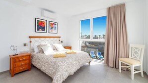 Ein Schlafzimmer mit Bett, Nachttischen, einem Sessel, einem Fenster mit Blick und Kunstwerken an der Wand.