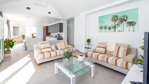 Ein modernes Wohnzimmer mit zwei Sofas, einem Glastisch und einer Küche im Hintergrund.