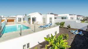 Ein moderner Poolbereich auf dem Dach mit klarem, blauem Wasser, umgeben von weißen Gebäuden und ausgestattet mit Liegestühlen und einem Glasgeländer.