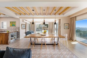 Un comedor moderno con una mesa de madera, sillas transparentes y lámparas colgantes.