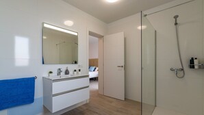 A modern bathroom with a glass shower enclosure, a white vanity with a mirror, and a blue towel on the wall. - Villa La Nueva by Villa Plus (Playa Blanca)