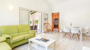A living room with a green sofa, a white coffee table, and a dining area with white chairs and a wooden cabinet. - Villa Luna by Villa Plus (Cap d'Artrutx)