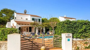 Una villa de dos pisos con piscina, mobiliario exterior y un muro de piedra.